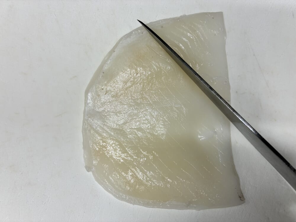 イカフライの油はねを防ぐため、開いたイカの胴体の内側に包丁で斜めの切り込みを入れている様子