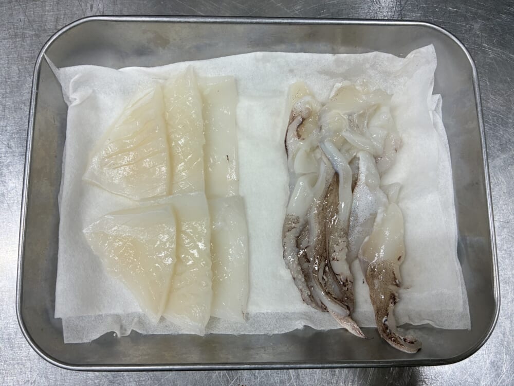 切り分けと吸盤処理を終えキッチンペーパーを敷いたバットに並べたイカの身とゲソ