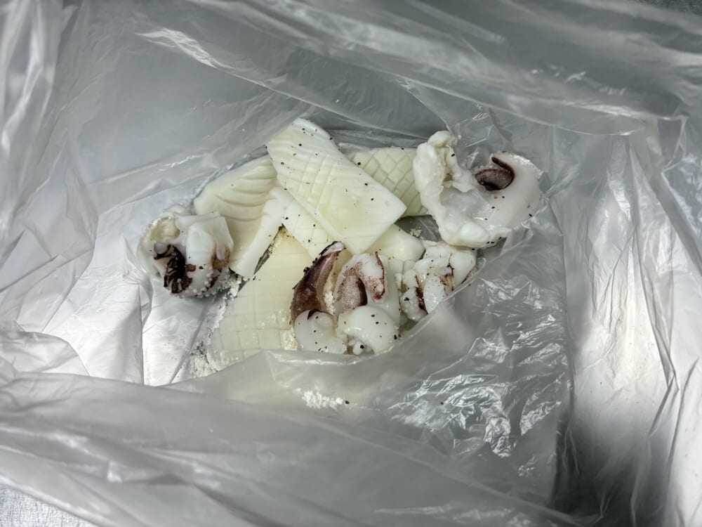 衣が剥がれないよう、ポリ袋の中にイカと小麦粉を入れて全体に薄く粉(打粉)をまぶす様子
