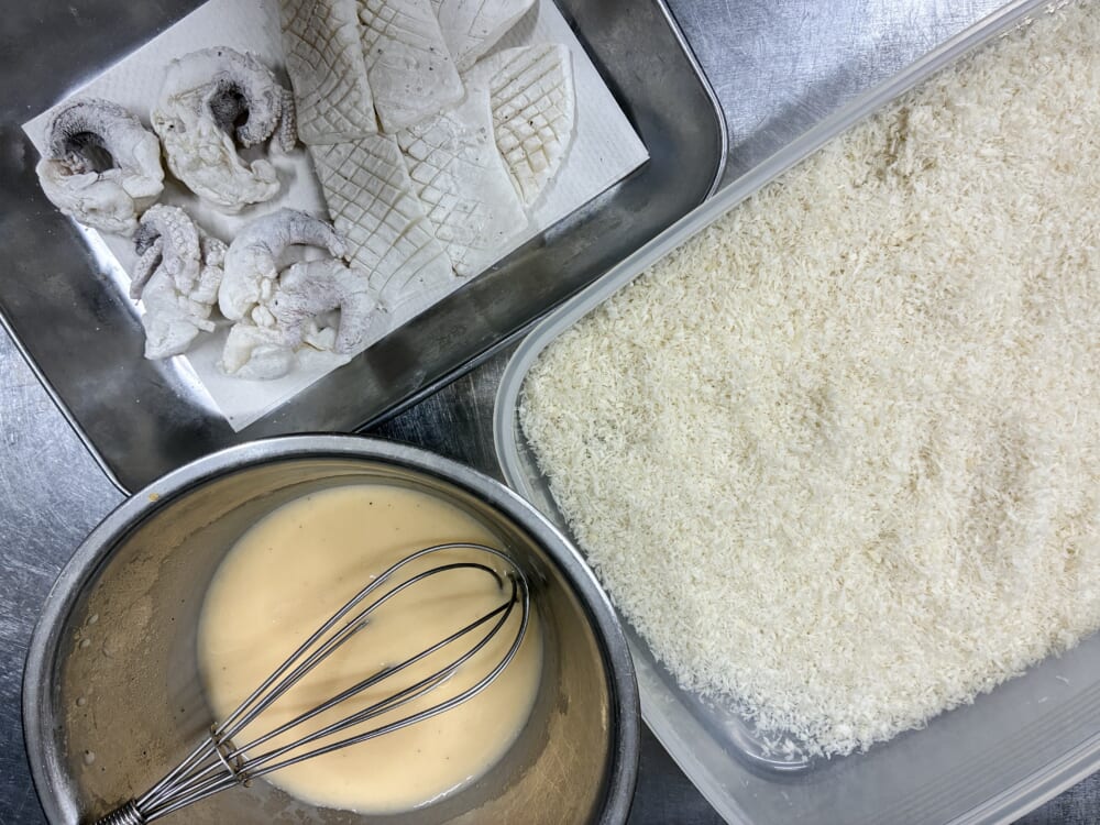 打粉をしたイカ、ボウルに合わせたバッター液、生パン粉を並べて衣付けの準備を整えたキッチン